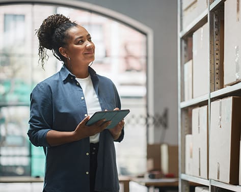 Portrait of a Worker Checking Inventory, Writing in Tablet Computer. Black Woman Working in a Warehouse Storeroom with Rows of Shelves Full of Parcels, Packages with Orders Ready for Shipment.